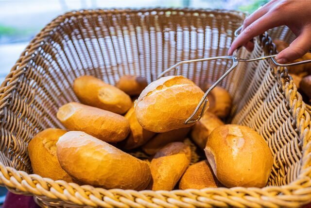 Eine Verkäuferin nimmt ein Brötchen mit einer Zange aus einem Brötchenkorb.