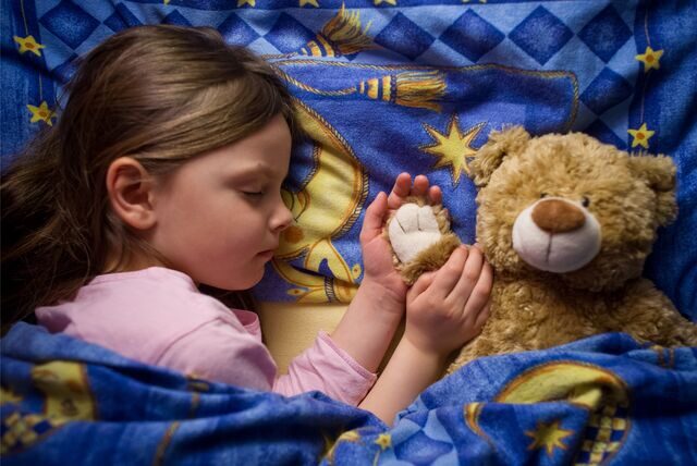 Ein Mädchen schläft mit einem Teddybären im Bett.