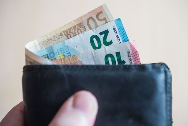Geldscheine im Wert von zehn, zwanzig, und fünfzig Euro stecken in einem Geldbeutel, der von einer Hand gehalten wird.