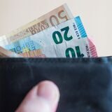 Geldscheine im Wert von zehn, zwanzig, und fünfzig Euro stecken in einem Geldbeutel, der von einer Hand gehalten wird.