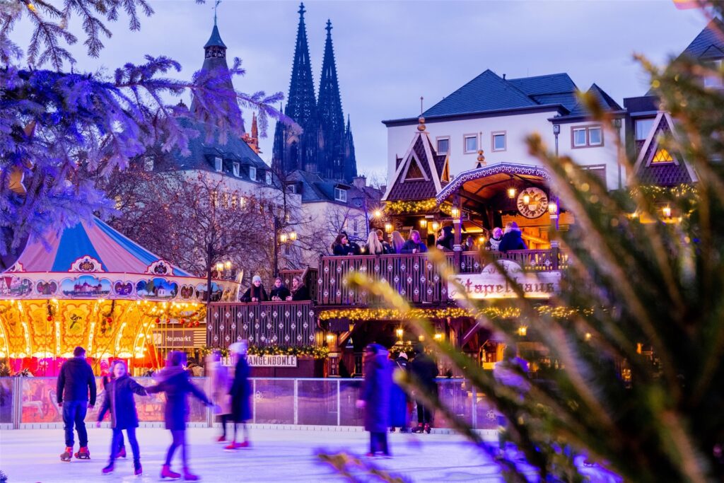 Besucher fahren auf der Eisbahn beim Weihnachtsmarkt am Heumarkt in Köln Schlittschuh. Besucher fahren auf der Eisbahn beim Weihnachtsmarkt am Heumarkt in Köln Schlittschuh.