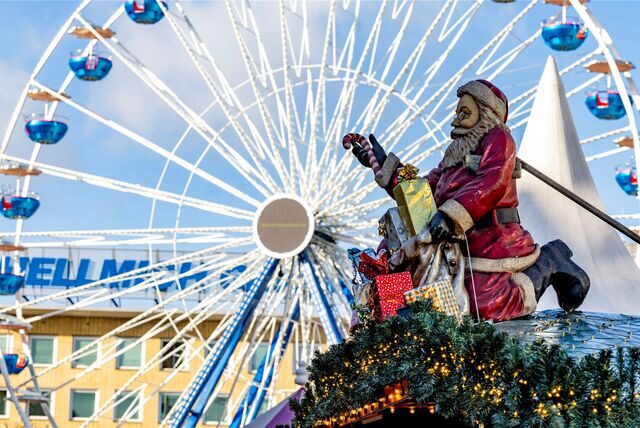 Ein Nikolaus mit Geschenken sitzt beim Weihnachtsmarkt in Duisburg auf dem Dach einer Glühweinhütte.