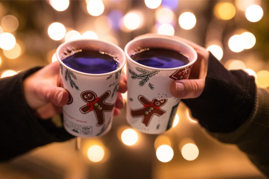 Zwei Frauen stoßen auf einem Weihnachtsmarkt mit Glühwein in Bechern an. Zwei Frauen stoßen auf einem Weihnachtsmarkt mit Glühwein in Bechern an.