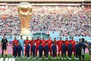 Spieler des Iran stehen beim Abspielen der Nationalhymne vor dem übergroßen Weltpokal im Stadion in Katar.