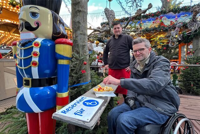Christian Baran isst auf dem Weihnachtsmarkt eine Pommes an einem Tisch für Rollstuhlfahrer.