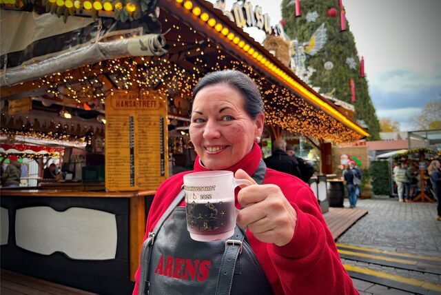 Luise Arens steht vor ihrem Glühweinstand auf dem Dortmunder Weihnachtsmarkt und hält eine Tasse mit Glühwein in der Hand.