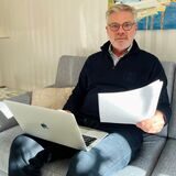 Olaf Bauer sitzt auf dem Sofa und hält seinen neuen Grundsteuerbescheid in der Hand.