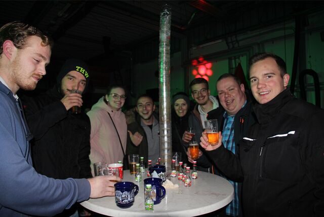 Eine Gruppe Menschen steht um einen Stehtisch herum, auf dem Glühweintassen, Kurze und Biergläser stehen.