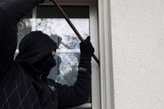 Ein Einbrecher hebelt ein Fenster auf. (Symbolbild)