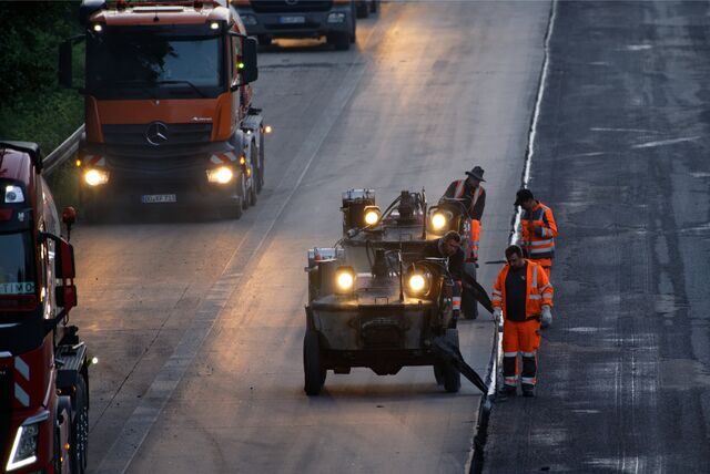 Arbeiter bringen mit schweren Maschinen den von Lastwagen gelieferten Asphalt auf die die Fahrbahn der A3 auf.