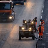 Arbeiter bringen mit schweren Maschinen den von Lastwagen gelieferten Asphalt auf die die Fahrbahn der A3 auf.