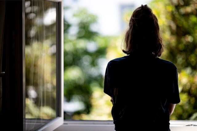 Eine Frau steht an einem Fenster und blickt hinaus.