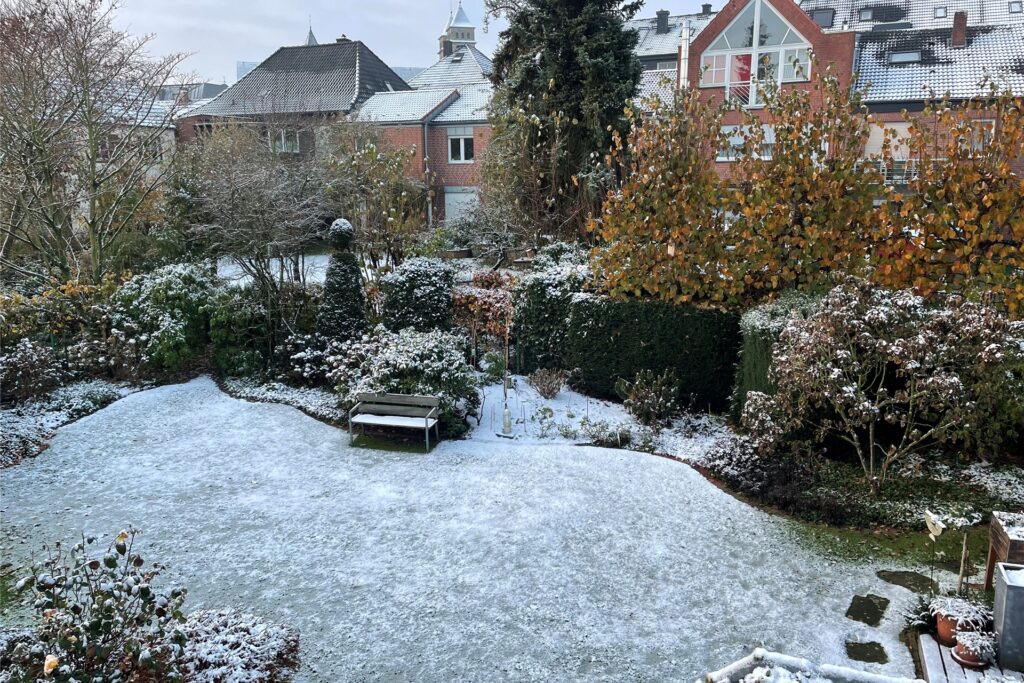 Leichter Schnee bedeckt einen Garten mit einer Bank. Leichter Schnee bedeckt einen Garten mit einer Bank.
