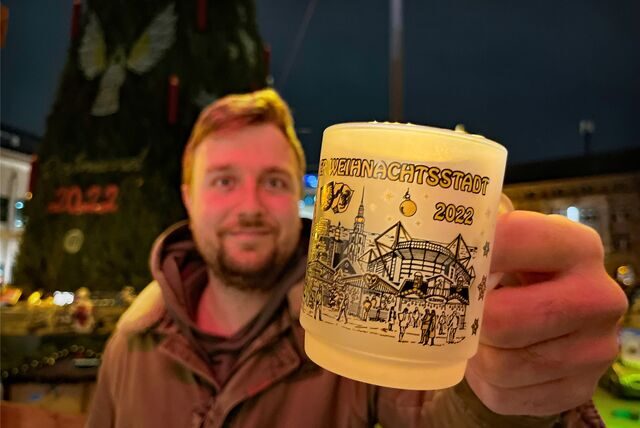Ein Mann hält die Dortmunder Weihnachtstasse 2022 in der Hand. Im Hintergrund der Dortmunder Weihnachtsmarkt.