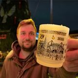 Ein Mann hält die Dortmunder Weihnachtstasse 2022 in der Hand. Im Hintergrund der Dortmunder Weihnachtsmarkt.