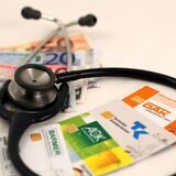 Die Versichertenkarten der Krankenkassen DAK, AOK, Barmer und Techniker-Krankenkasse TK liegen mit Euro-Geldnoten unter einem Stethoskop, aufgenommen am 17.12.2009.