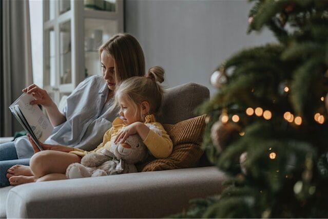 mutter liest ihrem kind auf der couch vorm weihnachtsbaum vor