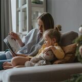 mutter liest ihrem kind auf der couch vorm weihnachtsbaum vor