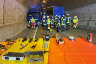 Einsatzkräfte der Feuerwehr stehen neben dem verunfallten Lkw