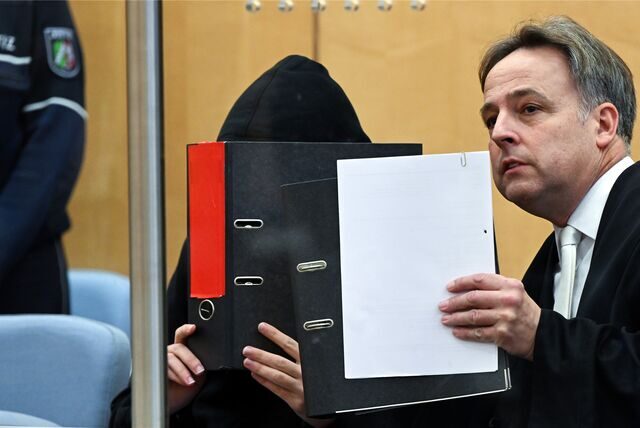 Der Angeklagte hält sich einen Aktenordner vor das Gesicht. Neben ihm sitzt sein Verteidiger.