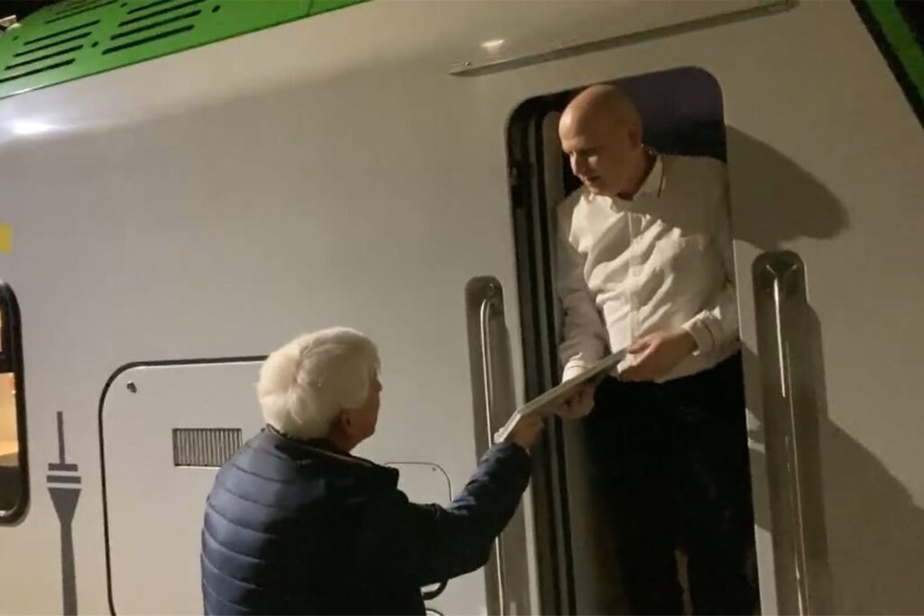 Straßenbahn-Fan Franz-Josef Hauke überreicht Lokführer Mike Kihm an der offenen Zugtür ein Exemplar des Buches 