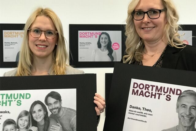 Jana-Larissa Marx (DEW21) und Jennifer Rickers (Stadtmarketing) halten ein paar der Plakate, mit denen die Stadt Dortmund für das Energiesparen werben will.