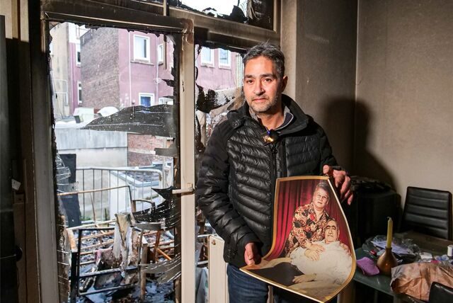 Mieter Hakan Saydan steht vor der von einem Feuer zerstörten Balkontür seiner Wohnung in Recklinghausen. In den Händen hält er ein Foto seiner Eltern.