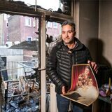 Mieter Hakan Saydan steht vor der von einem Feuer zerstörten Balkontür seiner Wohnung in Recklinghausen. In den Händen hält er ein Foto seiner Eltern.
