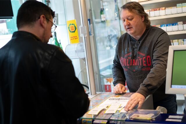 Ein Mann nimmt in einem Lotto-Laden einen Tippschein entgegen.