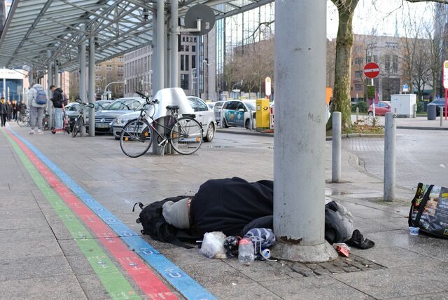 Ein wohnungsloser Mensch liegt unter einem Glasdach vor dem Dortmunder Hauptbahnhof.