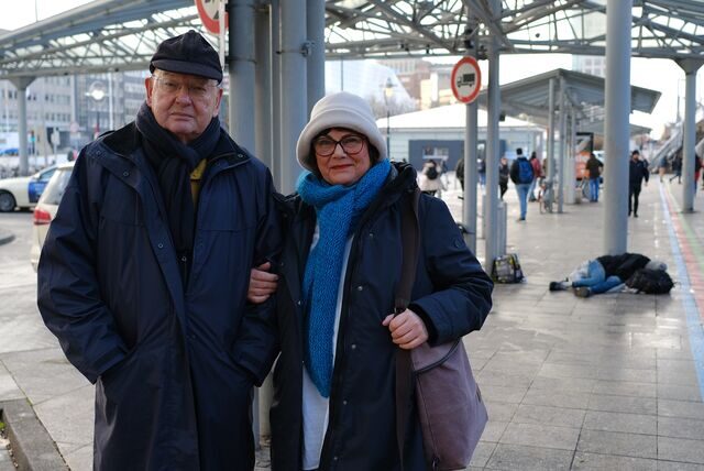 Peter und Brigitte Rösler unter der Überdachung am Taxistand am Dortmunder Hauptbahnhof. Im Hintergrund liegt ein wohnungsloser Mensch.