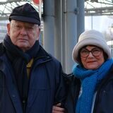 Peter und Brigitte Rösler unter der Überdachung am Taxistand am Dortmunder Hauptbahnhof. Im Hintergrund liegt ein wohnungsloser Mensch.