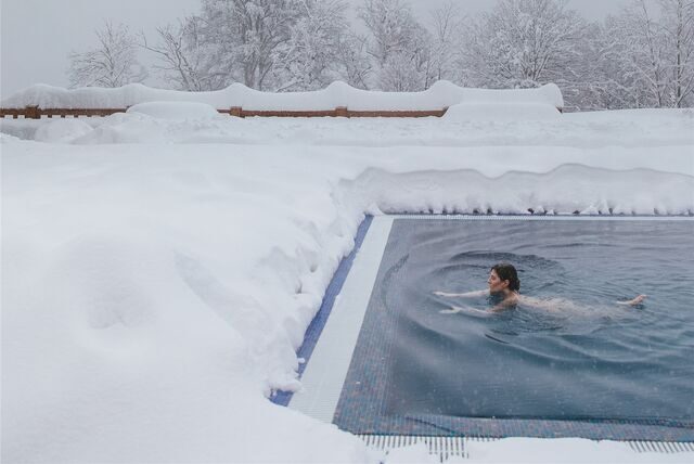frau schwimmt im pool währenddessen um sie herum überall schnee zu sehen ist