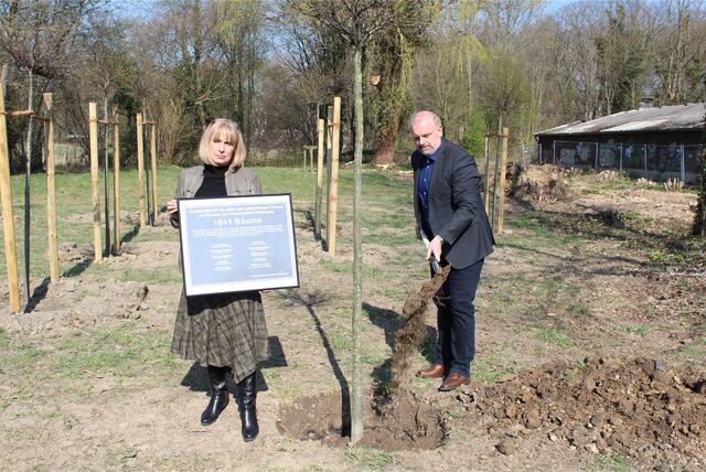 Bürgermeister Dirk Wigant pflanzte 2022 den elften Baum an der Gedenkstätte „10+1“, während  Ksenija Sakelsek, Vorsitzende des Integrationsrats, die Gedenktafel zeigte.