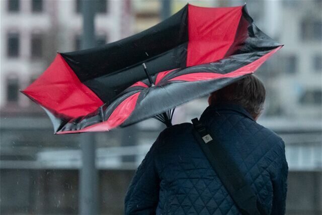 Ein Mann hält einen Regenschirm, der durch eine Windböe nach oben gedrückt wird.
