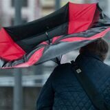 Ein Mann hält einen Regenschirm, der durch eine Windböe nach oben gedrückt wird.