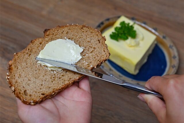 Eine Person streicht Butter auf eine Scheibe Brot.