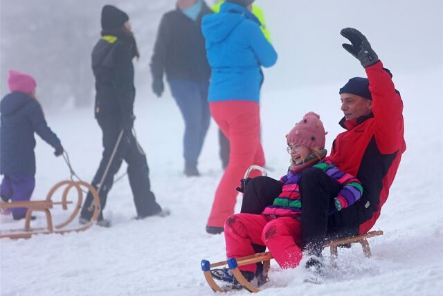 Ein Kind und ein Mann rodeln mit einem Schlitten durch den Schnee.