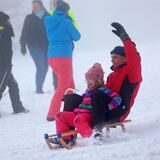 Ein Kind und ein Mann rodeln mit einem Schlitten durch den Schnee.
