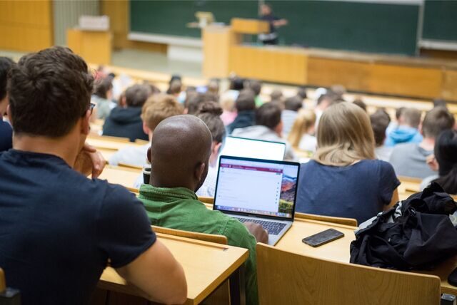 Studierende sitzen mit Laptops in einer Vorlesung.