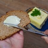 Eine Person bestreicht eine Scheibe Brot mit Butter.