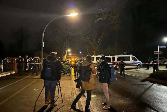 Polizisten und Flatterband im Hintergrund, davor drei Journalisten.