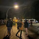 Polizisten und Flatterband im Hintergrund, davor drei Journalisten.
