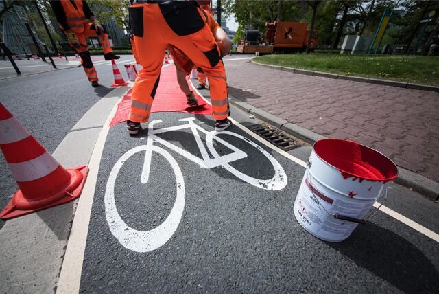 Ein Bauarbeiter markiert einen Radweg in Rot.