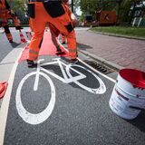 Ein Bauarbeiter markiert einen Radweg in Rot.