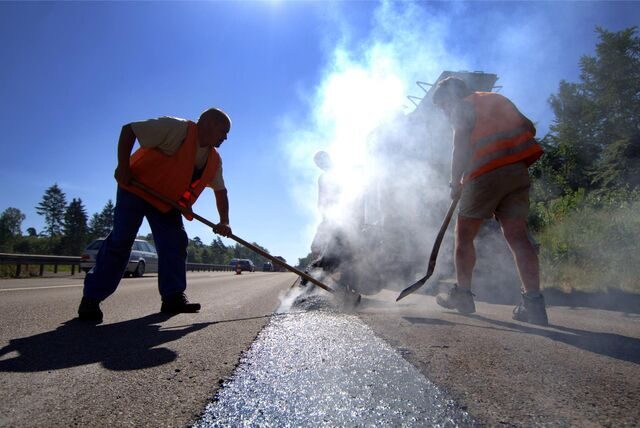 Straßenbauarbeiter verteilen kochenden Gussasphalt auf der Fahrbahn. (Symbolbild)