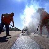 Straßenbauarbeiter verteilen kochenden Gussasphalt auf der Fahrbahn. (Symbolbild)