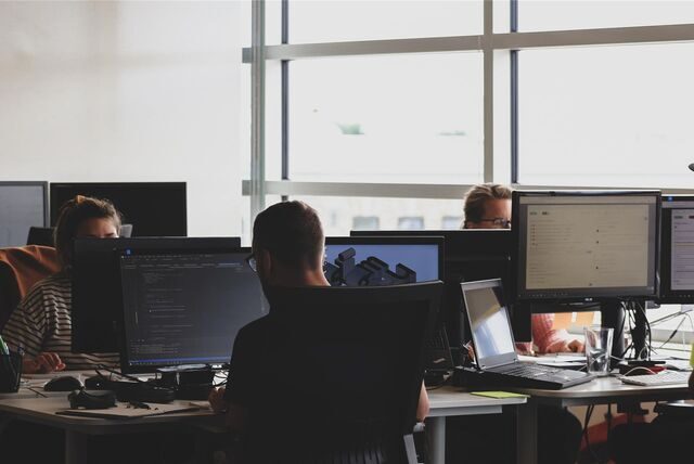 Drei Menschen sitzen in einem Büro an Computern.