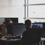 Drei Menschen sitzen in einem Büro an Computern.
