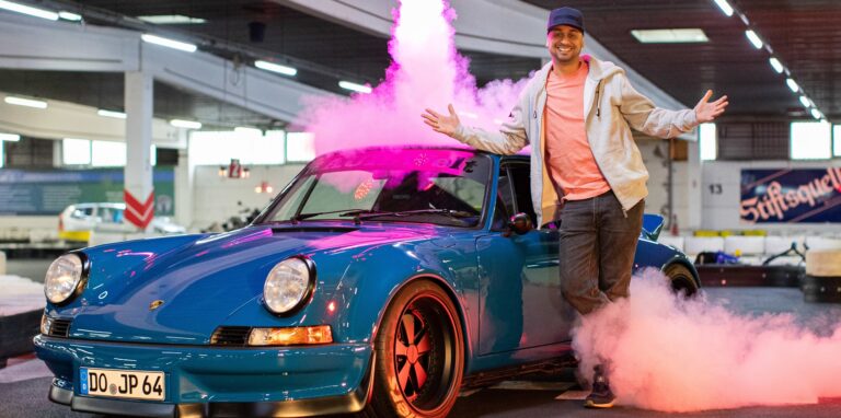 JP Kraemer vor einem blauen Sportwagen und Feuerwerk